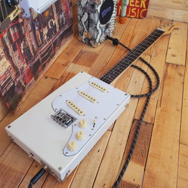 Guitare cigar box 4 cordes électrique blanche "De Luxe". Configuration stratocaster avec manche et érable et touche en ébène. Guitare cigar box 4 cordes électrique blanche "De Luxe". Configuration stratocaster avec manche et érable et touche en ébène.