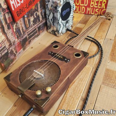 Guitare cigar box acoustique 3 cordes avec résonator scie circulaire, micro simple bobinage et finition brun vintage. Guitare cigar box acoustique 3 cordes avec résonator scie circulaire, micro simple bobinage et finition brun vintage.