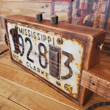 Guitare cigar box électrique réalisée avec une boite sur mesure et une plaque d'immatriculation américaine rouillée Mississippi. Guitare cigar box électrique réalisée avec une boite sur mesure et une plaque d'immatriculation américaine rouillée Mississippi.