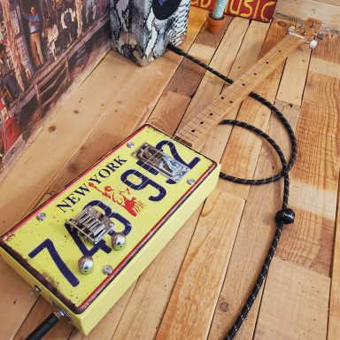Guitare cigar box électrique jaune réalisée avec une plaque d'immatriculation américaine.