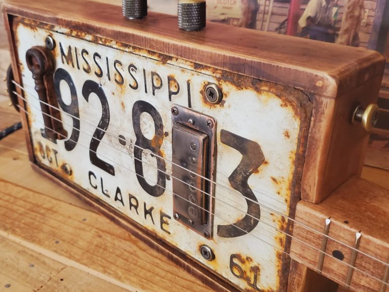 Guitare cigar box 3 cordes réalisée avec une plaque d'immatriculation rouillée du Mississippi. Guitare cigar box 3 cordes réalisée avec une plaque d'immatriculation rouillée du Mississippi.